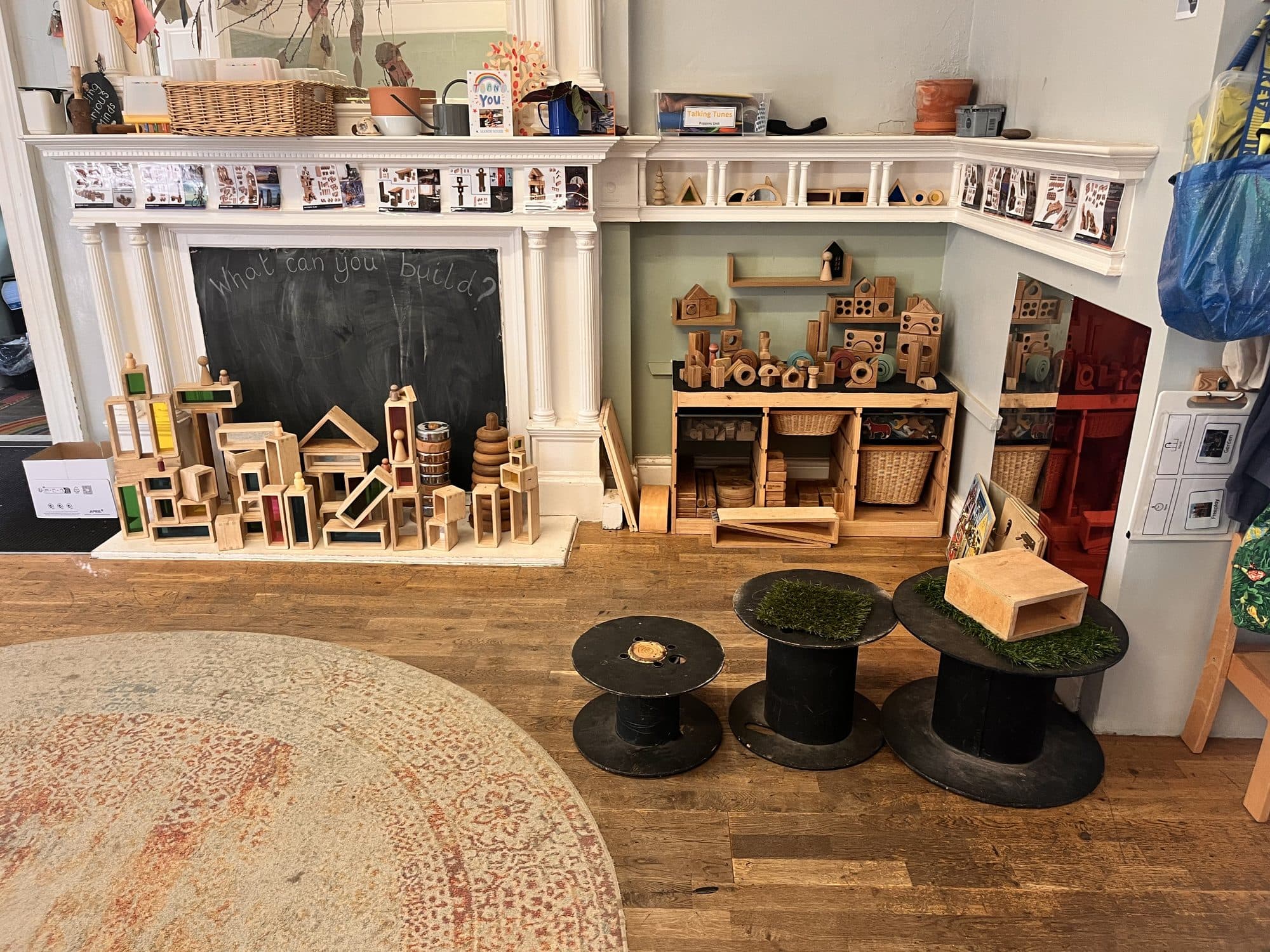 A playroom with a fireplace, wooden blocks and cable reel tables at The Manor House Nursery, Bristol
