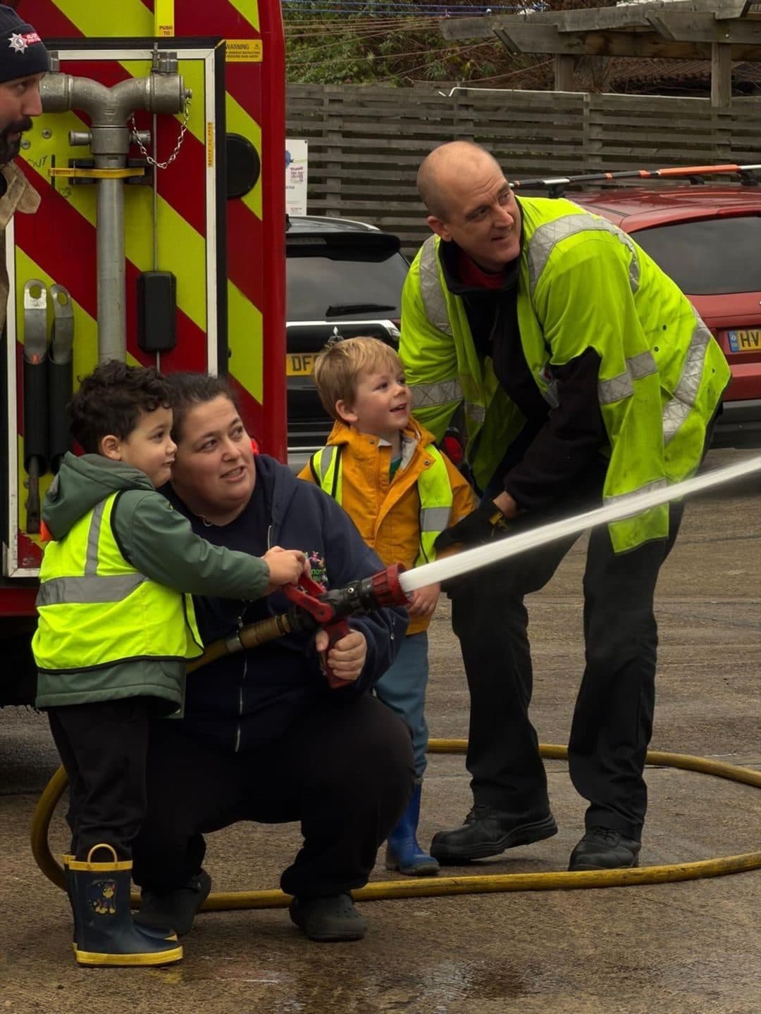 Children trying a fire hose during a fire crew visit to The Manor House Nursery, Westbury on Trym