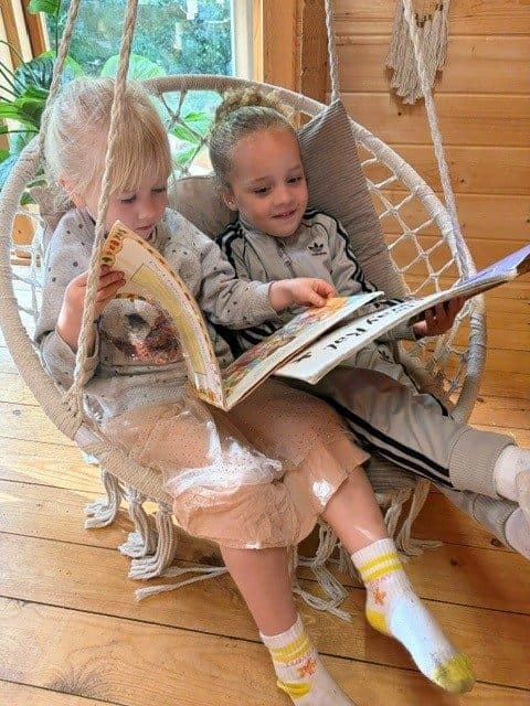 Two children sharing a book in a hanging seat at The Manor House Nursery in Westbury on Trym