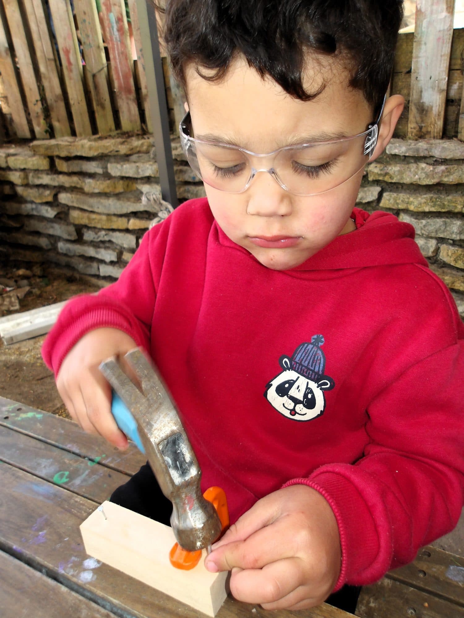 A child using a real hammer at the woodworking bench at The Manor House Nursery, Westbury on Trym